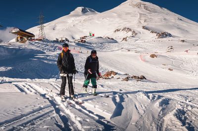 Pair of skiers standing on skis side by side in a helmet and goggles getting ready for the descent