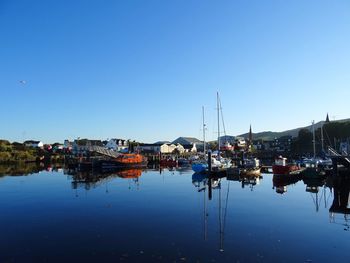 Boats moored at harbor against clear blue sky