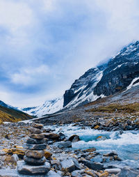 Scenic view of cairn by the flowing stream between mountains against sky.