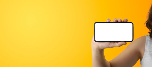 Midsection of person holding smart phone against yellow wall