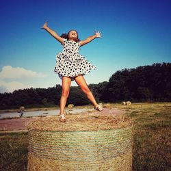 Full length of carefree girl with arms outstretched standing on hay bale