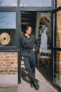 Female owner standing with legs crossed at ankle while looking away at boutique doorway