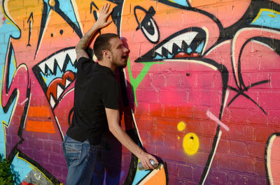 Full length of young man standing against graffiti wall