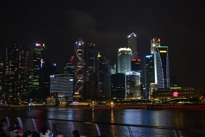 Crowd by river against illuminated buildings in city