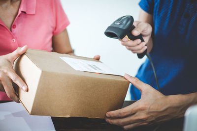 Midsection of male worker scanning barcode on package held by woman