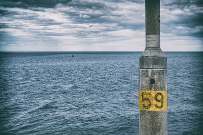 Number on pole in sea against sky