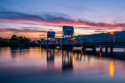 Bridge over river against sky at sunset