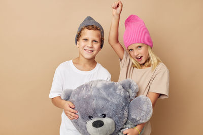 Portrait of sibling holding stuffed toy against beige background