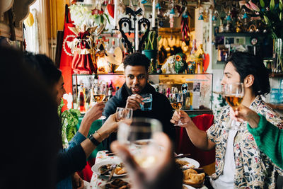Cheerful young multi-ethnic friends raising toast while sitting at table in restaurant