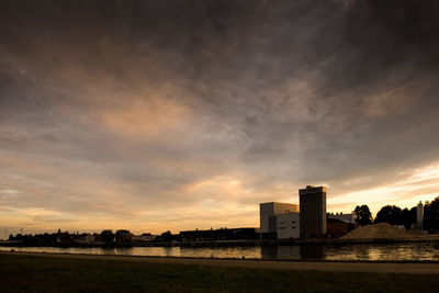 Buildings by river against sky during sunset