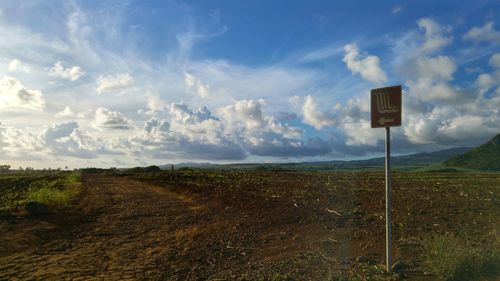 Road sign on field against sky