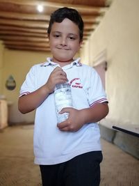 Portrait of boy holding water bottle while standing at home