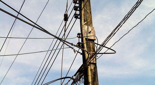 Low angle view of electricity pylon against cloudy sky