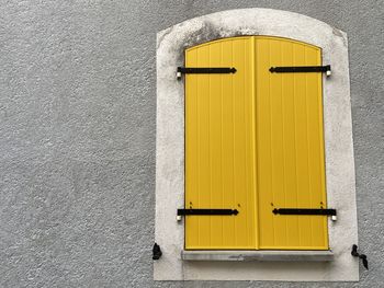 Window with closed yellow wooden shutters on the grey wall of the house