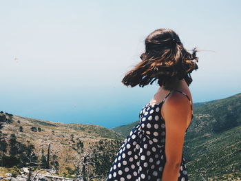 Side view of woman standing on mountain against sky during sunny day