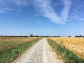 Empty road amidst field against sky