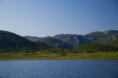 Scenic view of lake and mountains against clear blue sky