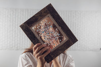 Portrait of woman covering face with picture frame at home