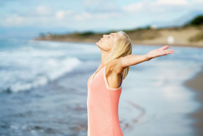 Senior woman with arms outstretched standing at beach