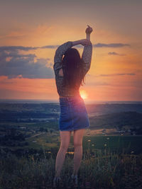 Rear view of woman standing at beach against sky during sunset