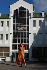 Glamorous urban photography, chic image of model in golden silk dress outdoors posing near building 