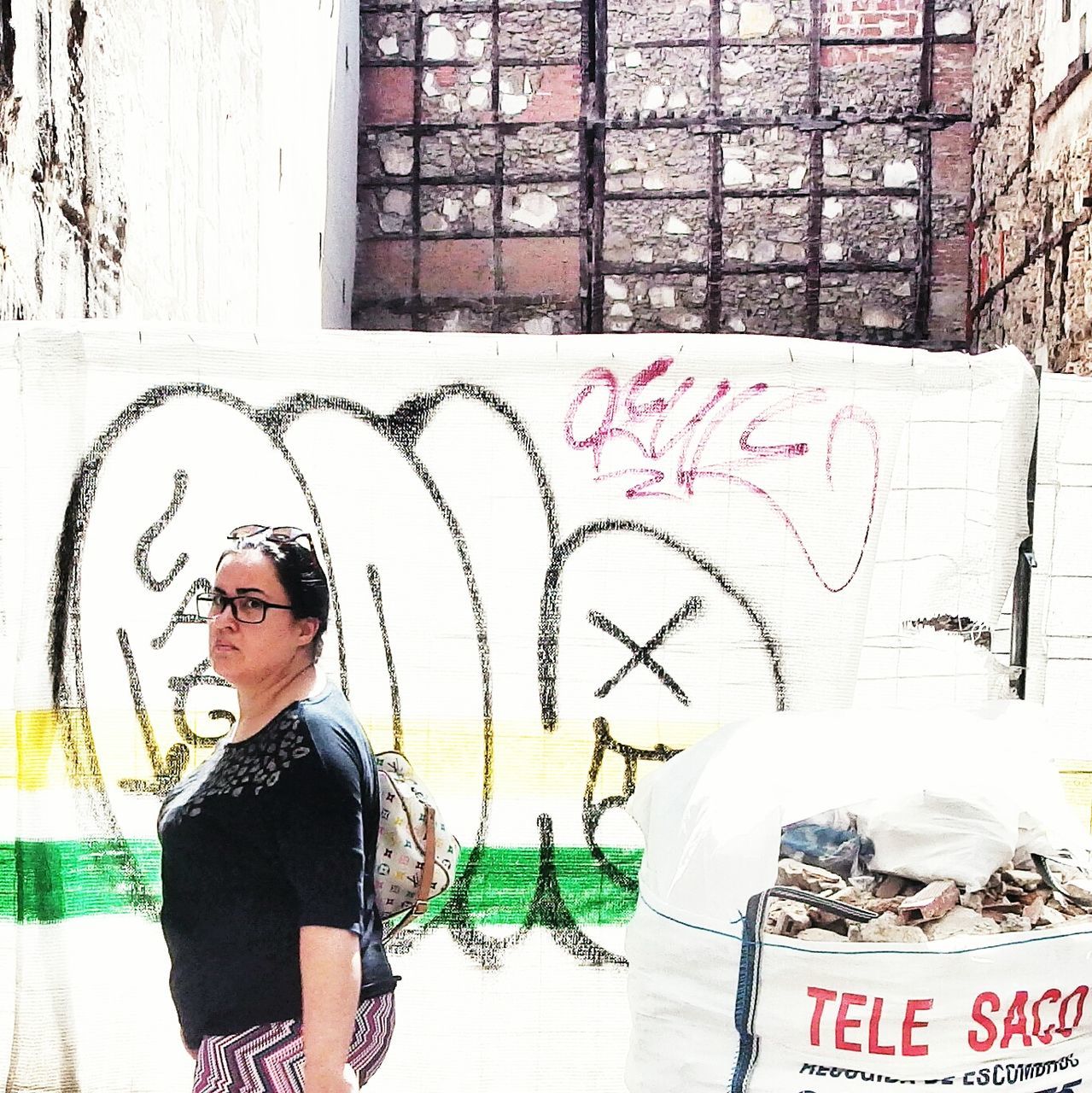 lifestyles, young adult, text, communication, person, leisure activity, front view, wall - building feature, casual clothing, standing, young women, looking at camera, three quarter length, graffiti, portrait, western script, sunglasses, smiling