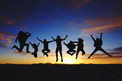Silhouette people jumping against sky during sunset