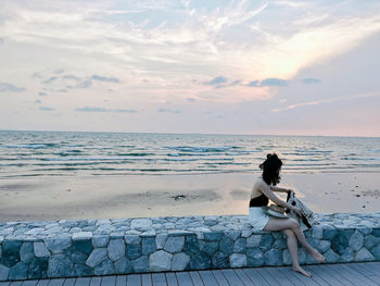 Woman sitting on beach by sea against sky