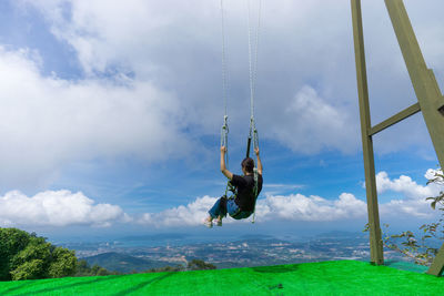 Rear view of woman swinging on swing against sky