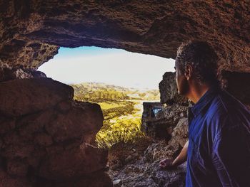Side view of man looking at mountains while standing under rock formation