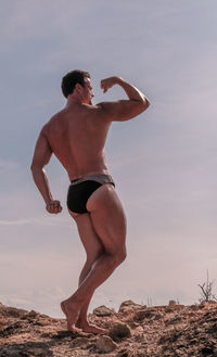 Full length of man flexing muscles against sky