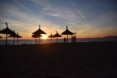 Silhouette parasols on beach against sky during sunset