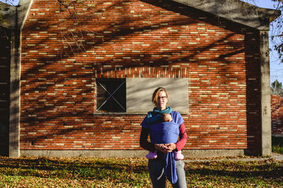 Portrait of woman with baby standing against house