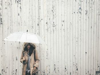 Woman holding umbrella while standing by corrugated iron