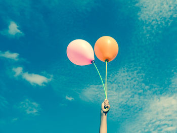 Low angle view of hand holding balloons against blue sky