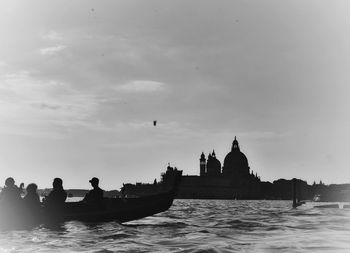 Silhouette of people on boat in city against sky