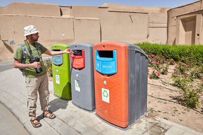 Man standing by garbage bin against wall