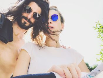 Low angle view of young couple wearing sunglasses sitting against sky