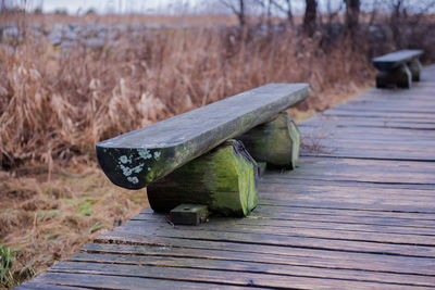 Empty wooden bench on boardwalk by field