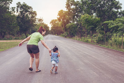 Rear view of woman with daughter walking on road amidst trees