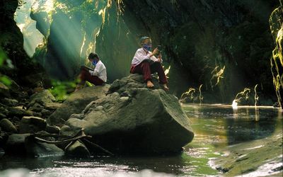 Full length of boys wearing mask sitting on rock at forest