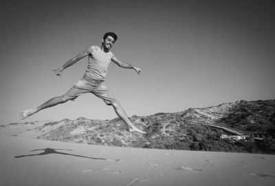 Smiling young man jumping on beach against clear sky