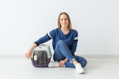 Portrait of smiling woman sitting on floor with cage