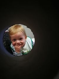 Portrait of cute smiling baby boy with fingers in mouth seen through window