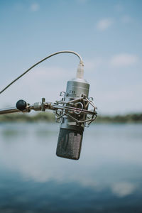 Close-up of microphone hanging by lake against sky