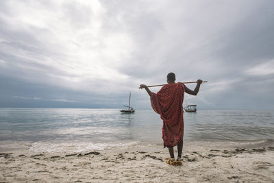Rear view of man standing at beach against sky