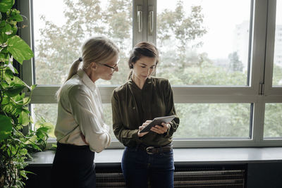 Two businesswomen using tablet in office at the window