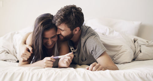 Man embracing woman holding home pregnancy test at home