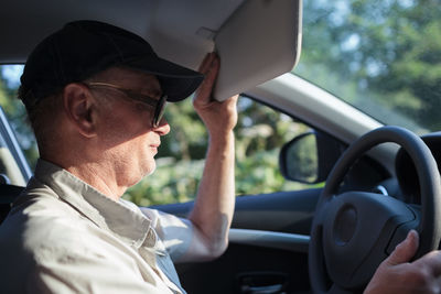 Side view of man holding sun visor in car