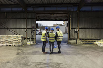 Full length rear view of manual workers discussing in cement warehouse